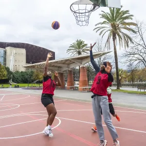 Two diverse women in red jerseys actively playing basketball on an outdoor court