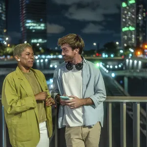 Diverse young couple chatting and smiling on an urban bridge at night Diverse young couple chatting and smiling on an urban bridge at night