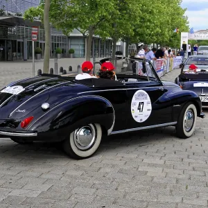 DKW F 93, black vintage convertible driving on a city street with green trees in the background