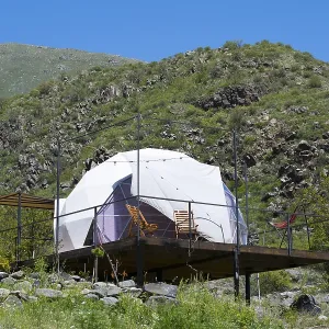 Dome tent on a wooden terrace in green mountain landscape under blue sky