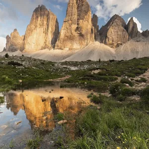 Dramatic Three Peaks rocks in the evening light are reflected in a small pond with wild flowers
