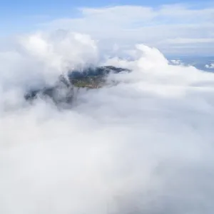 Dramatic view of mountains rising from clouds under blue sky