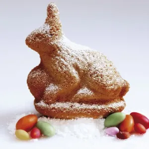 Easter bunny made of sponge cake sitting on icing sugar with Easter sweets