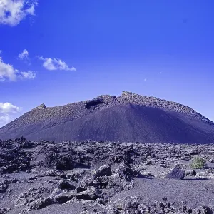 The El Cuervo volcano (Caldera de los Cuervos) rises above a lava field under a clear blue sky