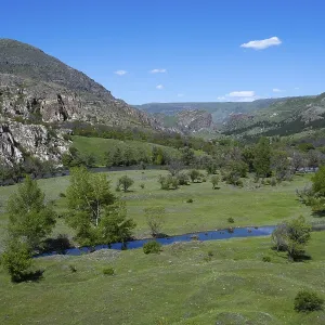 Extensive green valley with a small river and hill background