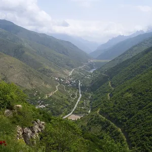 Extensive mountain landscape with a river surrounded by lush vegetation and clouds in the sky