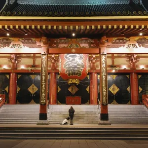 Famous Tokyo landmark, Asakusa Temple colorful entrance by night with silhouettes of prayer woman and big dog