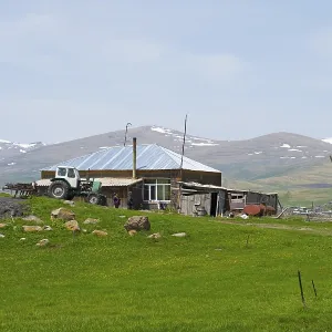 A farm with tractors and a stone house in front of a mountain landscape