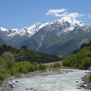 Fast-flowing river in a wooded valley against a backdrop of snow-capped mountains