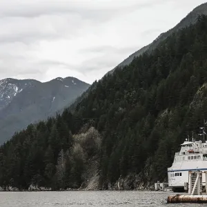 A ferry navigating near mountains covered in dense forest under cloudy skies at Horseshoe Bay A ferry navigating near mountains covered in dense forest under cloudy skies at Horseshoe Bay