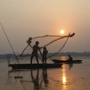 Fishermen in boat throwing net in silhouette