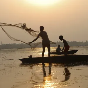 Fishermen in boat throwing net in silhouette