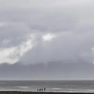 Foggy beach view with dark clouds and distant figures under mountains along the Lower Mainland of British Columbia