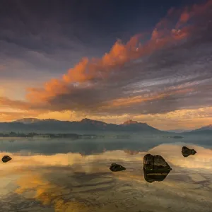 Forggensee with reflection of the cloudy sky and the Allgaeuer mountains in the background at sunrise