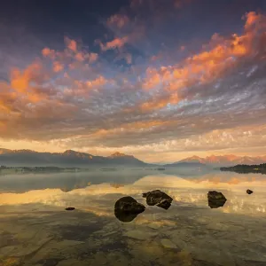 Forggensee with reflection of the cloudy sky and the Allgauer mountains in the background at sunrise Forggensee with reflection of the cloudy sky and the Allgauer mountains in the background at sunrise