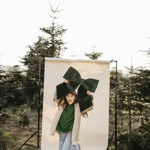 Girl holding green stitch standing in front of beige studio background in nature