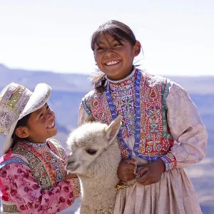 Two girls in traditional dress with an alpaca