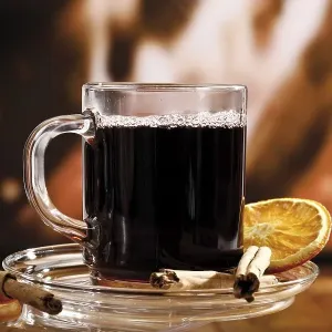 Glass of mulled wine garnished with cinnamon sticks and a dried orange slice in front of a fireplace