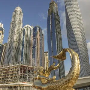 Golden sculpture in front of modern skyscrapers under blue sky