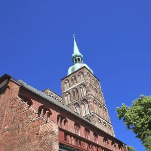 Gothic brick church tower against a clear blue sky next to green trees