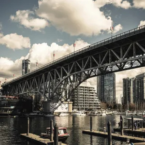 A grand bridge stretches over a busy harbor against a backdrop of clouds in Vancouver A grand bridge stretches over a busy harbor against a backdrop of clouds in Vancouver