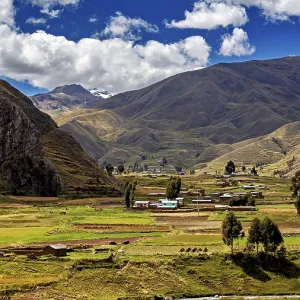 Green fields and hills against a mountain backdrop under a cloudy blue sky