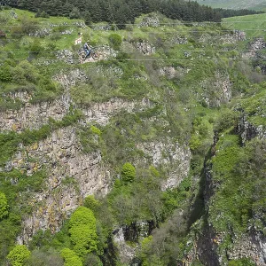 A green gorge with rocks and trees crossed by a small river under a cloudy sky A green gorge with rocks and trees crossed by a small river under a cloudy sky
