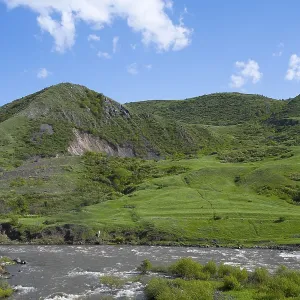 Green hills and a river under a blue sky offer a peaceful landscape