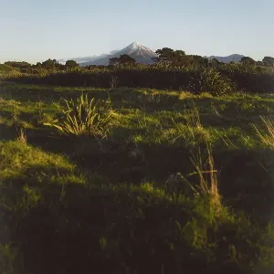 A green hilly landscape under a clear blue sky with a mountain peak in the background creating a peaceful atmosphere A green hilly landscape under a clear blue sky with a mountain peak in the background creating a peaceful atmosphere
