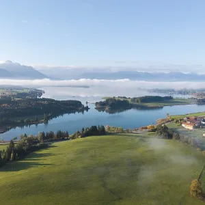 Green hilly landscape with quiet Forggensee and light fog