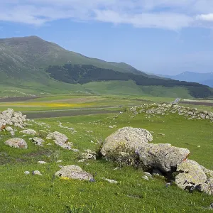 Green hilly landscape with rocks and mountains in the background under a slightly cloudy sky Green hilly landscape with rocks and mountains in the background under a slightly cloudy sky