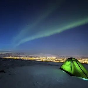 Green illuminated tent in the snow and aurora borealis above Fjellheisen