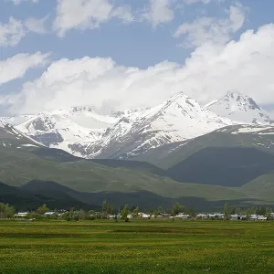 Green meadows in front of snow-covered mountains under a cloudy blue sky Green meadows in front of snow-covered mountains under a cloudy blue sky