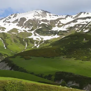 Green mountain landscape with snow and clouds in the sky