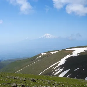 Green mountain landscape with snowfields and cloudy sky in the distance