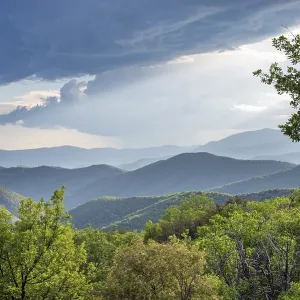 Montañas verdes y valles que se estiran hasta el horizonte bajo un cielo dramático con rayos de luz.