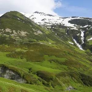 Green mountains with waterfalls and snow under a blue sky