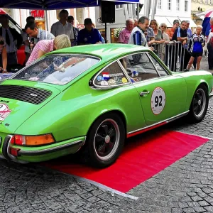 A green Porsche classic car stands on a red carpet surrounded by people