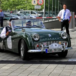 Green vintage convertible with two occupants driving on paved road