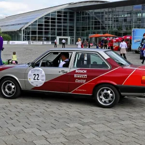 Grey-red car at a vintage car event with modern architecture in the background