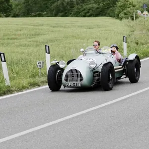 A grey vintage racing car drives on a rural road through green nature A grey vintage racing car drives on a rural road through green nature