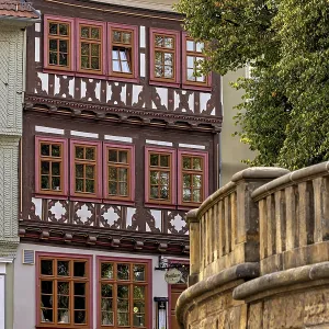 A half-timbered house with red window frames next to a stone wall in a historic town A half-timbered house with red window frames next to a stone wall in a historic town