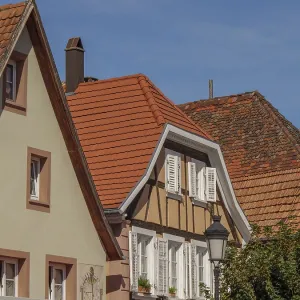 Three half-timbered houses with red tiled roofs and white shutters under a blue sky