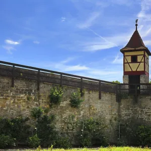 Tour en bois de façade sur haute muraille urbaine sous ciel clair avec verdure environnante.