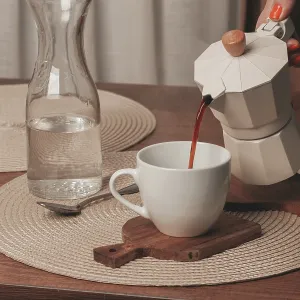A hand pours freshly brewed coffee from a stovetop maker into a white cup A hand pours freshly brewed coffee from a stovetop maker into a white cup
