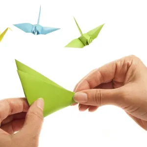 Hands crafting an origami piece with colorful cranes in the background