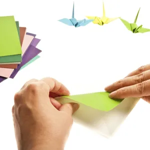 Hands folding green origami with colorful paper cranes in the background