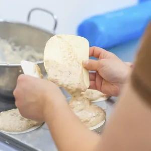 Two hands working with a dough and a silicone spatula on a kitchen table