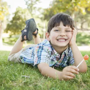 Handsome young boy enjoying his lollipop outdoors on the grass