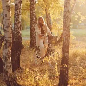 Happy active young woman riding vintage bicycle in autumn park at sunset